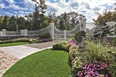 a white fence surrounded by lush green grass next to a stone walkway and flower garden