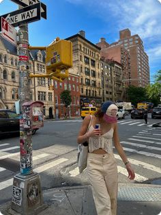 a woman walking across a street next to a traffic light and cross walk sign with buildings in the background