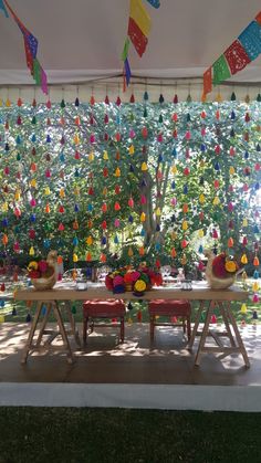 the table is set for two with colorful decorations hanging from the ceiling and trees in the background