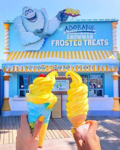 someone holding up two ice cream cones in front of a frozen treat shop with an image of a gorilla on it