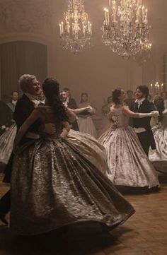 two people dancing in formal dress with chandeliers