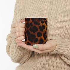 a woman's hand holding a leopard print coffee mug in front of her face