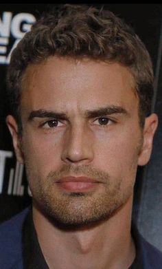 a close up of a person wearing a suit and tie with short hair in front of a black background