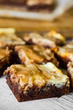 some brownies with cheese on top of them sitting on a wooden table next to a cutting board