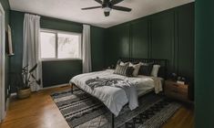 a bedroom with dark green walls and white bedding, wooden flooring and ceiling fan