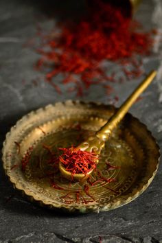 a gold plate with a spoon and some red saffroni seeds on it