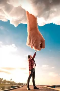 a person holding up a giant hand with the sky in the background and clouds above