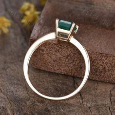 a close up of a ring with a green stone in it on top of a piece of wood