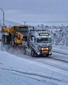 a large truck driving down a snow covered road next to a yellow dumptruck