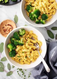 two bowls filled with pasta and broccoli on top of a marble countertop