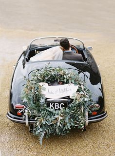 the bride and groom are sitting in an old black car with a wreath on it