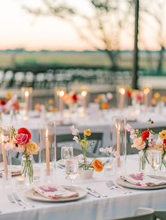 the table is set with white linens and colorful flowers in glass vases on each side