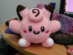 a pink stuffed animal sitting on top of a wooden table next to a computer monitor