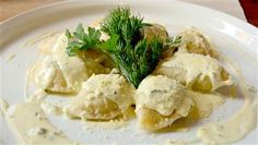 a white plate topped with ravioli covered in sauce and garnished with parsley