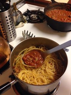 spaghetti being cooked in a pan on the stove top with other cooking utensils