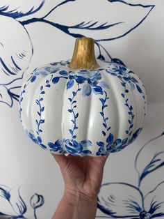 a white and blue painted pumpkin being held in front of a wallpapered background