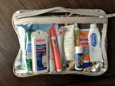 the contents of a travel bag sitting on a wooden floor, including toothbrushes and lotion