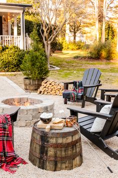 an outdoor fire pit surrounded by chairs and tables with blankets on them in front of a house