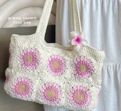 a crocheted purse with pink flowers on the front and white handles, hanging from a hook