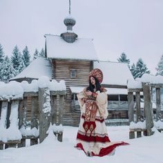 a woman standing in front of a log cabin wearing a traditional dress and headdress