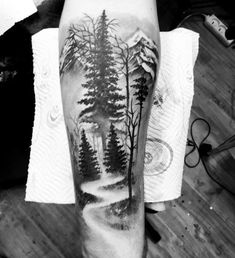 a black and white photo of trees on the arm with mountains in the background tattoo