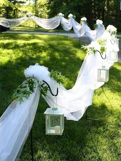 some white lanterns are set up in the grass for an outdoor wedding ceremony with greenery on them