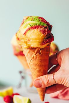 a hand holding an ice cream cone with raspberries and limes in the background