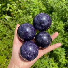 three purple eggs sitting on top of someone's hand in front of some bushes