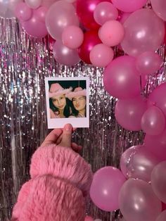 a person holding up a polaroid photo in front of pink and silver foil balloons