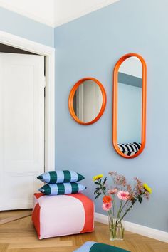 a living room with blue walls and orange mirrors on the wall next to a flower vase