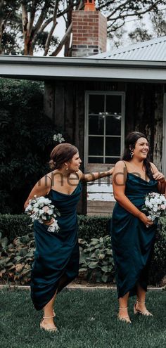 two bridesmaids laughing in front of a house with their bouquets on the grass