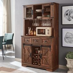 a wooden cabinet with wine glasses on top and a microwave in the middle, sitting next to a dining room table