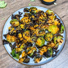 a white plate topped with cooked brussel sprouts next to a bowl of sauce