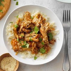 a white plate topped with rice covered in meat and cilantro next to a wooden spoon