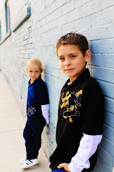 two young boys leaning against a brick wall