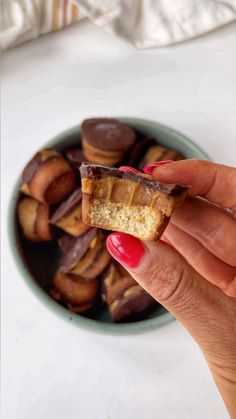 a hand holding a piece of food over a bowl of desserts on a table