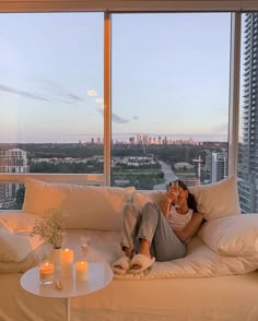 a woman sitting on top of a white couch next to a window with city view