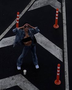 a woman standing in the middle of an orange and white striped road with traffic cones