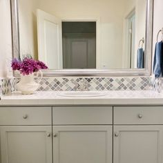 a bathroom vanity with a large mirror above it and flowers in the vase on the counter