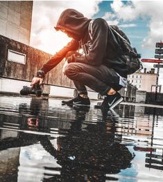 a man squatting down on the ground in front of a puddle