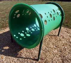 a green metal bucket sitting on top of a dirt field next to a fence and grass covered field