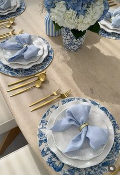 the table is set with blue and white plates, napkins, and gold place settings