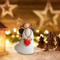 a small angel figurine holding a heart in front of a christmas tree with lights