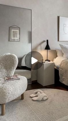 a bedroom with a bed, chair and mirror in it's corner on the floor