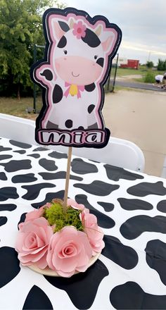 there is a cake topper with a cow on it and pink flowers in the foreground