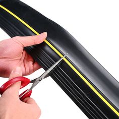 a person cutting through the side of a black tire with a pair of red scissors