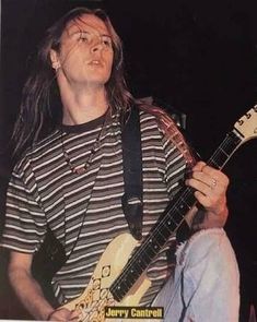 a man with long hair playing a guitar in front of a microphone and wearing a striped shirt