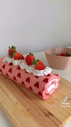 a strawberry roll with cream and strawberries on top sitting on a cutting board next to a bowl of strawberries