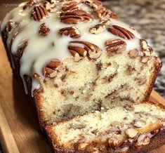 a loaf of cake with pecans and icing sitting on top of a cutting board