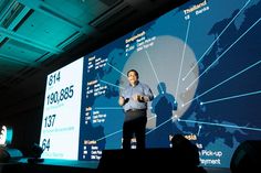 a man standing in front of a projection screen with his hands on his hips while talking